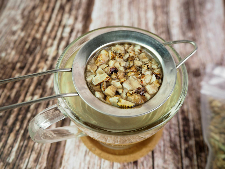 Frisch zubereiteter Kalmustee in einer Teetasse mit einem Teesieb, hervorhebend die gesundheitlichen Vorteile von Acorus calamus.